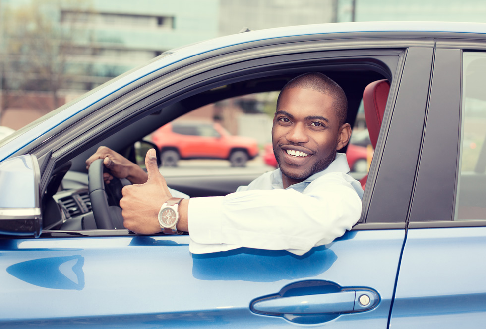 Young man sitting in the driver's seat of a car showing thumbs up