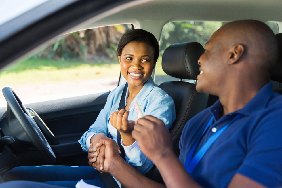 Young woman sitting in the passenger seat of a car shaking the hand of a driving instructor